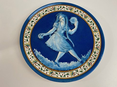 French faience plate / wall plaque with motif of blue girl with long braids in 
relief. The girl dances and plays music with castanets and tambourine, first 
half of the 20th century