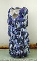 Christina Muff, dansk samtidskeramiker (f. 1971). Meget høj og slank unika 
skulpturel vase, der åbner op til den ene side øverst. Denne vase er glaseret i 
et utal af blå toner, den er blevet brændt adskillige gange for at opnå denne 
effekt.