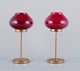 A pair of brass tealight holders in wine-red glass shades.