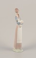 Lladro, Spanien. Porcelænsfigur af stående ung kvinde med lam i armene.