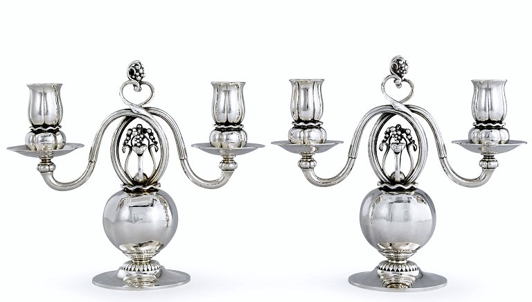 Georg Jensen. Et par Kandelabre af hammerslået sterlingsølv med to svungne 
lysarme, prydet med stiliseret ornamentik og drueklaser. 
Kandelaber 324 kaldes også for 