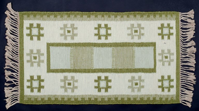 Swedish textile artist. Handwoven wool carpet in Rölakan technique. Modernist 
design. Green colors on a white background.